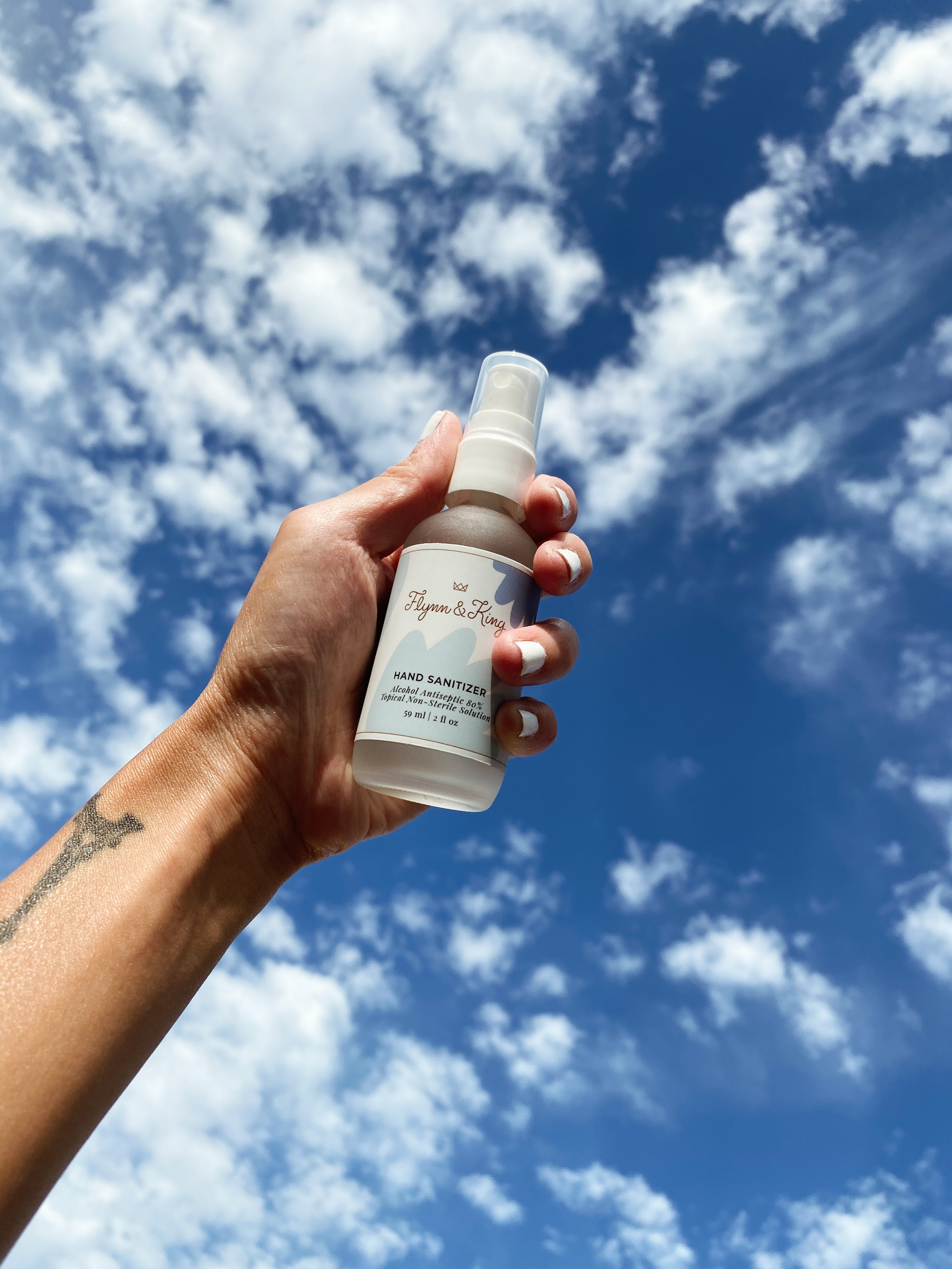 Hand holding a bottle of unscented hand sanitizer with a lovely sky and cloud background